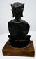 Crowned bronze Buddha with an upright seated posture, a rounded bronze seat, and a warm brown wooden display base.