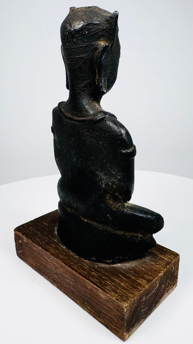 Bronze Buddha displaying curved back contours, projecting ear ornaments, and mottled surface wear above its wooden mount.