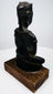 Bronze Buddha displaying curved back contours, projecting ear ornaments, and mottled surface wear above its wooden mount.