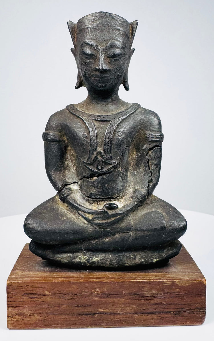 Crowned bronze Buddha seated with crossed legs and folded hands, mounted on a wooden base against a beige background.