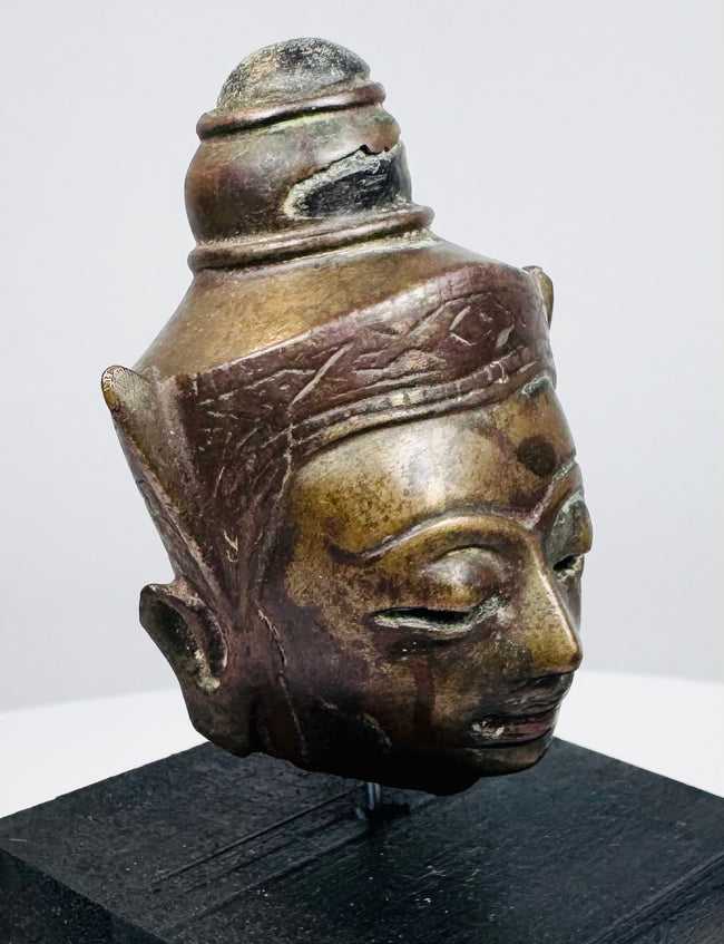 Small Southeast Asian metal Buddha head with detailed relief decoration and black wooden base