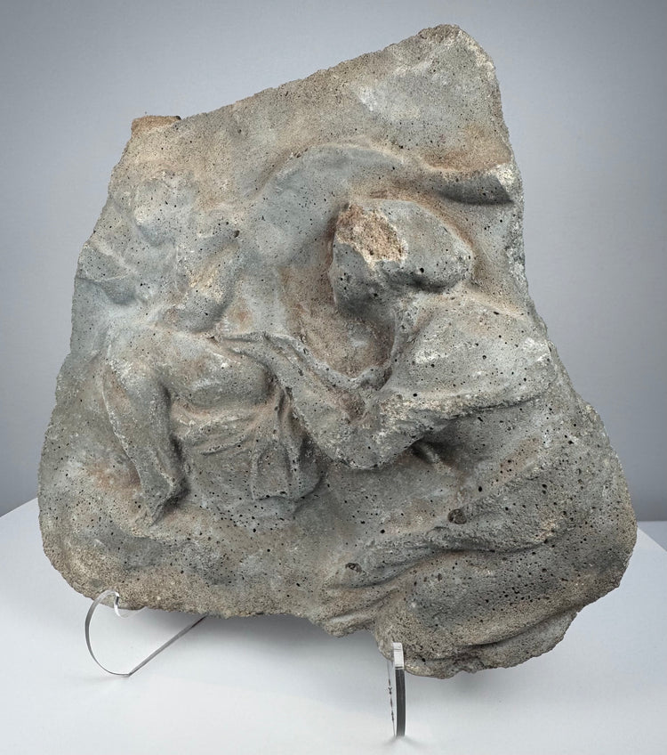 Roman relief fragment in gray volcanic tuff showing weathered human figures and naturally pitted stone surface