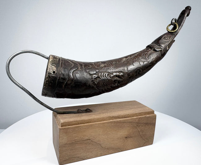 Angled view of a Tibetan carved horn ritual implement with decorative body motifs and opening for ritual use.