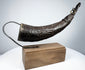 Angled view of a Tibetan carved horn ritual implement with decorative body motifs and opening for ritual use.