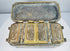 Interior of an antique Mindanao buyo box showing four decorated compartment lids arranged within the fitted metal case.