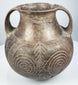 Early Etruscan impasto amphora with twin loop handles, flared rim, rounded body, and large incised spiral motifs across the front.
