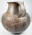 Etruscan terracotta amphora angled to show one handle opening, the short neck, rounded shoulder, and deeply incised spiral patterns.
