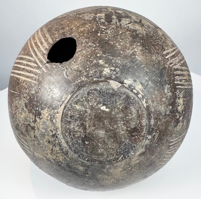 Ancient impasto amphora showing a side section with linear incisions, aged terracotta surface, and a visible vertical crack on the body.