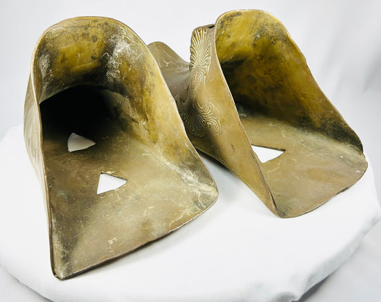 Ornate antique brass riding stirrups featuring stylized feathered headdress relief figure.