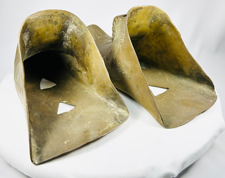 Ornate antique brass riding stirrups featuring stylized feathered headdress relief figure.