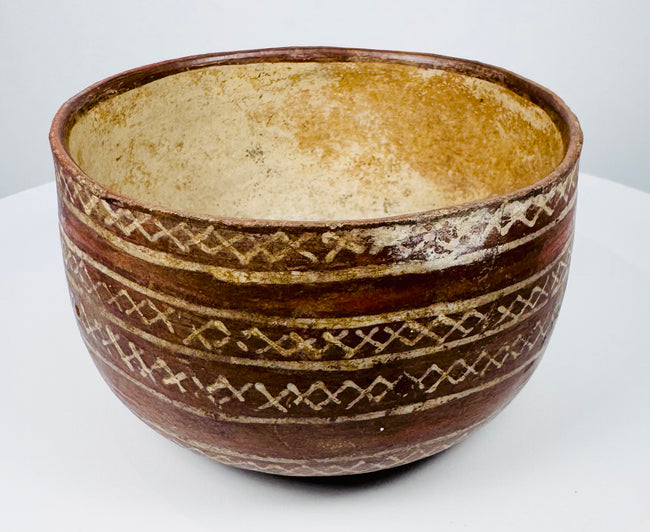 Bichrome pottery bowl featuring cream geometric ornament on a reddish-brown surface.
