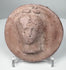 Ancient terracotta roundel from the Greek world showing a frontal female figure with classical features.