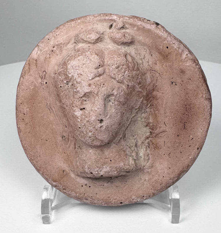 Ancient terracotta roundel from the Greek world showing a frontal female figure with classical features.