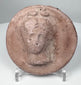 Ancient terracotta roundel from the Greek world showing a frontal female figure with classical features.