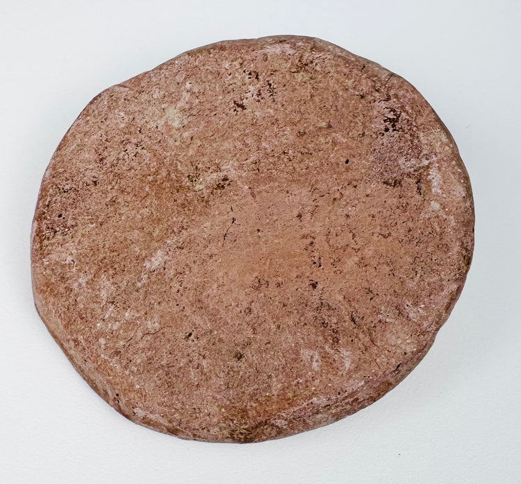 Reverse of a Hellenistic Greek terracotta female bust medallion showing the plain flattened back, aged pinkish-buff surface, mineral deposits, and edge wear.