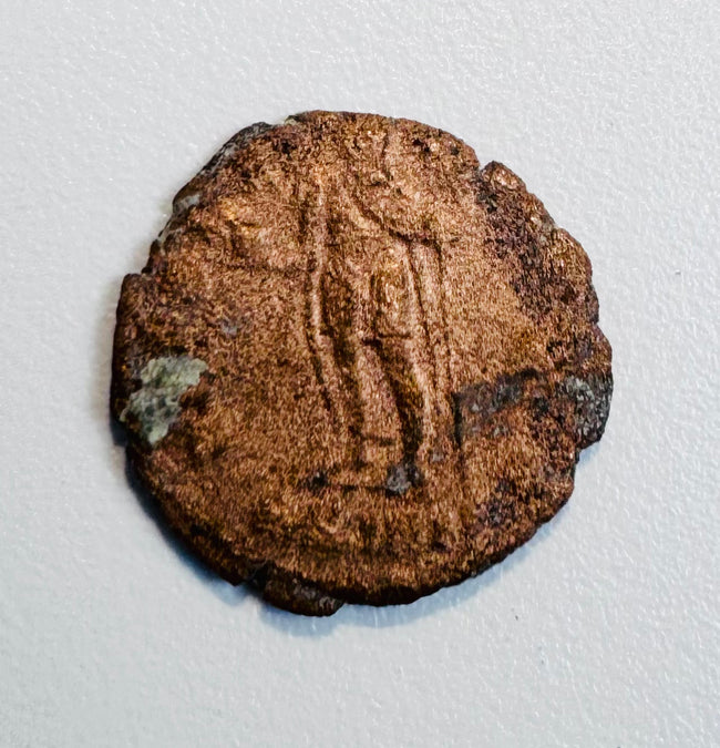 Late Roman copper-alloy coin with standing figure reverse, worn inscription, edge losses, and areas of green oxidation.
