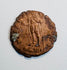 Late Roman copper-alloy coin with standing figure reverse, worn inscription, edge losses, and areas of green oxidation.