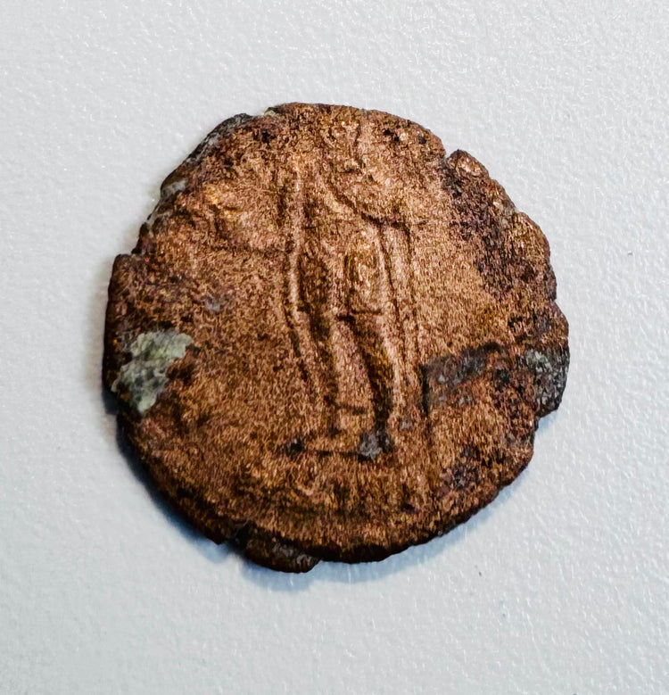 Late Roman copper-alloy coin with standing figure reverse, worn inscription, edge losses, and areas of green oxidation.