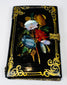Antique black lacquer card case with colorful floral inlay, gilt corner scrollwork, and brass closure