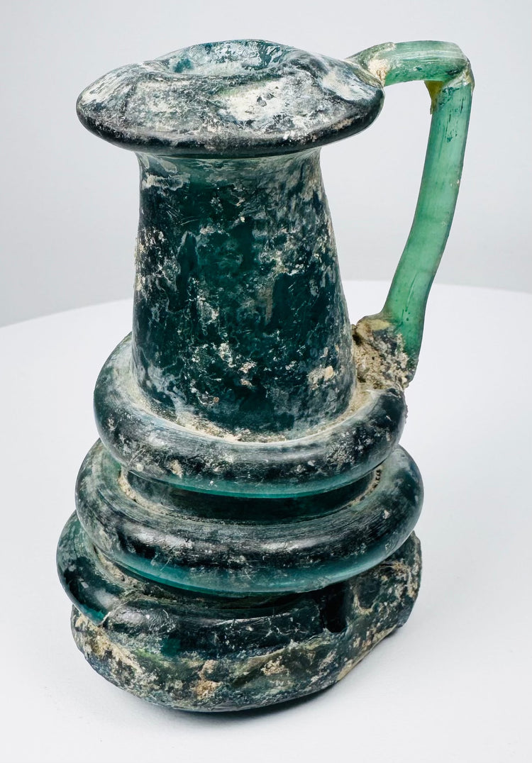 Ancient Roman blown-glass jug with rounded body, tall neck, and applied green glass handle