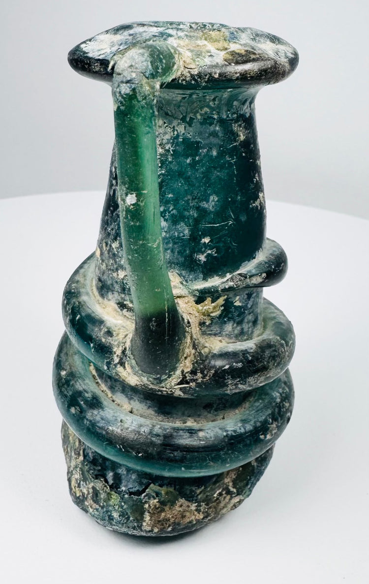 Late Roman green glass vessel showing applied handle, rounded body, and heavy burial deposits