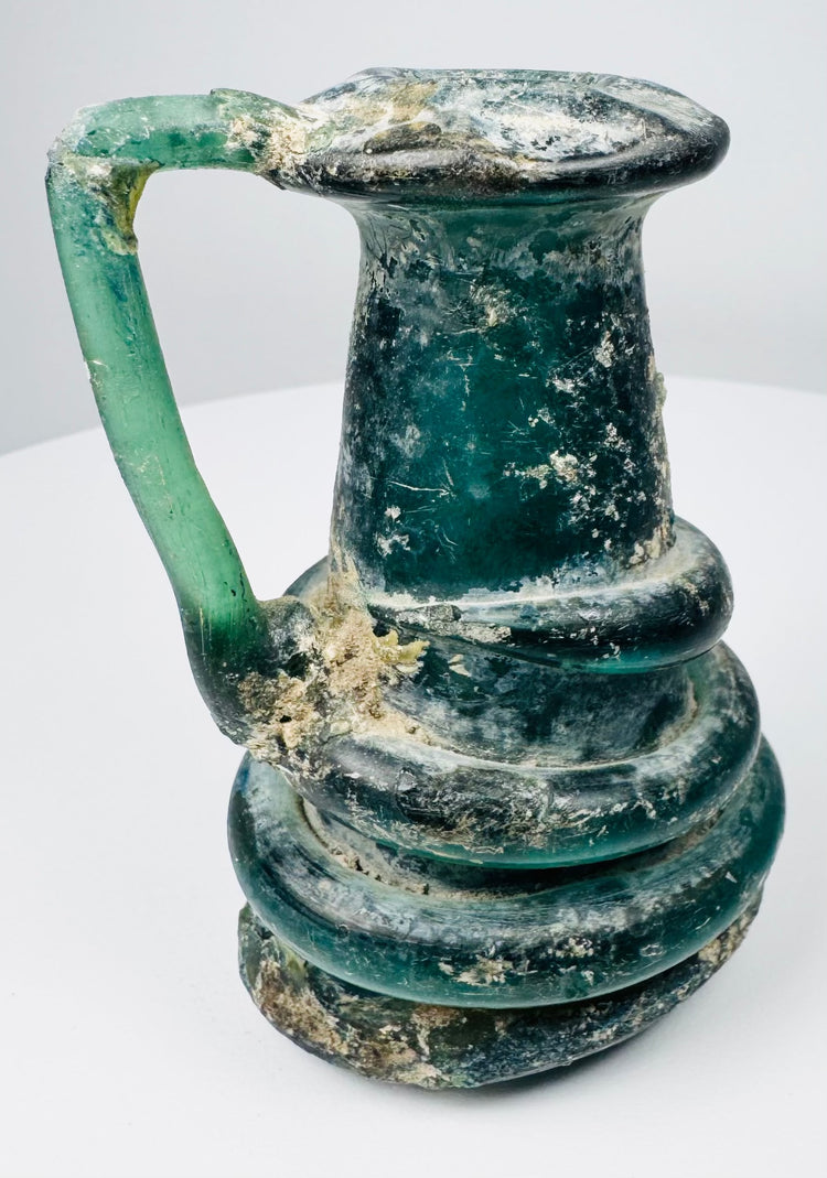 Ancient Roman green glass jug with flared rim, applied handle, and natural mineral encrustation