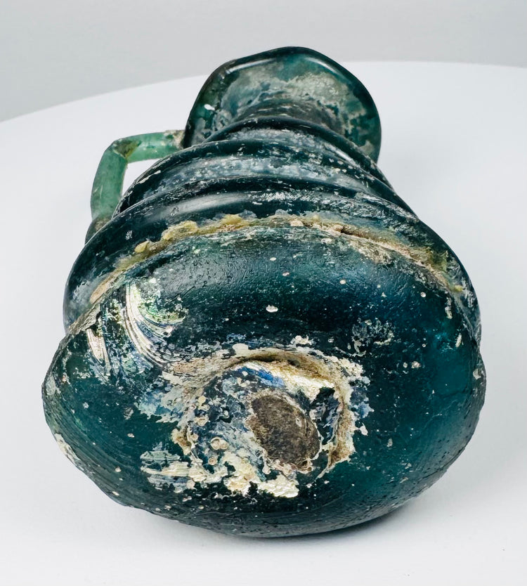 Underside of Late Roman blown-glass jug showing pontil scar, mineral deposits, and ancient glass weathering