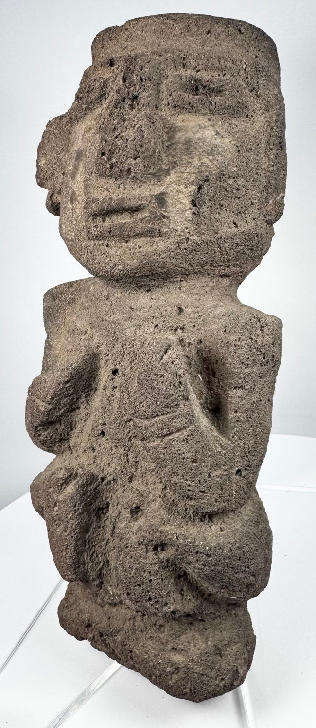 Pre-Columbian volcanic stone figure with recessed eyes, prominent brow, and stylized facial features