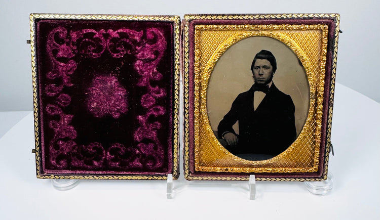 Antique male photographic portrait framed by an ornate gilt-metal oval mat and decorative burgundy velvet interior