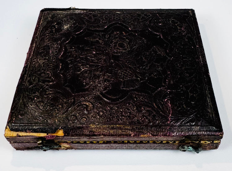 Mid-19th-century photographic case showing embossed floral ornament, worn spine, and original metal closure hardware