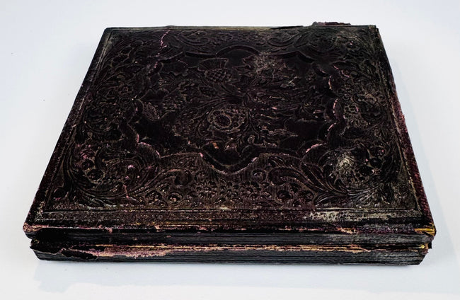 Antique cased photograph with ornate dark embossed exterior, decorative border, and age-related patina