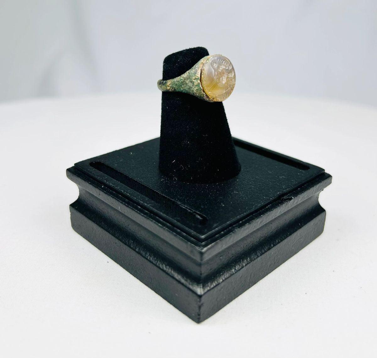Ancient Indo-Greek ring from modern Afghanistan, Pakistan, or Northern India, circa 2nd–1st Century BCE, featuring a carved garnet bezel depicting a bearded male bust in profile. The metal band shows natural patina, reflecting over 2,000 years of history and the Hellenistic-Indian artistic fusion of the Indo-Greek Kingdom.