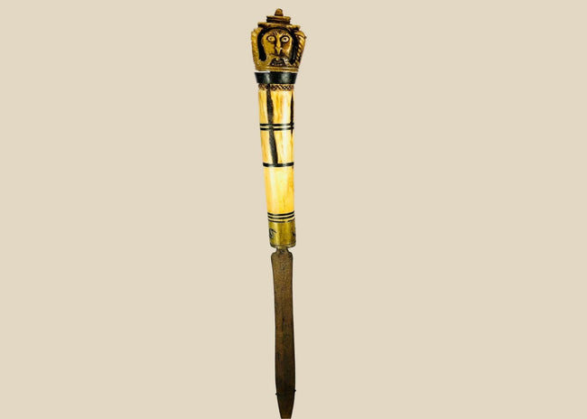 Indonesian Dayak knife from 19th century with carved bone handle depicting an Aso guardian beast and a male figure with elaborate mustache, steel blade, patinated surface, reflecting ritual and cultural significance of Borneo craftsmanship.