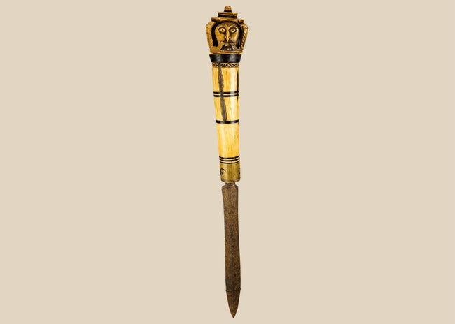 Indonesian Dayak knife from 19th century with carved bone handle depicting an Aso guardian beast and a male figure with elaborate mustache, steel blade, patinated surface, reflecting ritual and cultural significance of Borneo craftsmanship.