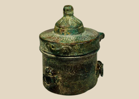 Antique Islamic Khorassan bronze inkwell, cylindrical form with domed lid, engraved with intricate geometric and vegetal motifs, rich green patina from centuries of age, dating to the 10th–12th century, historically used by Islamic scholars and scribes as part of manuscript tradition.