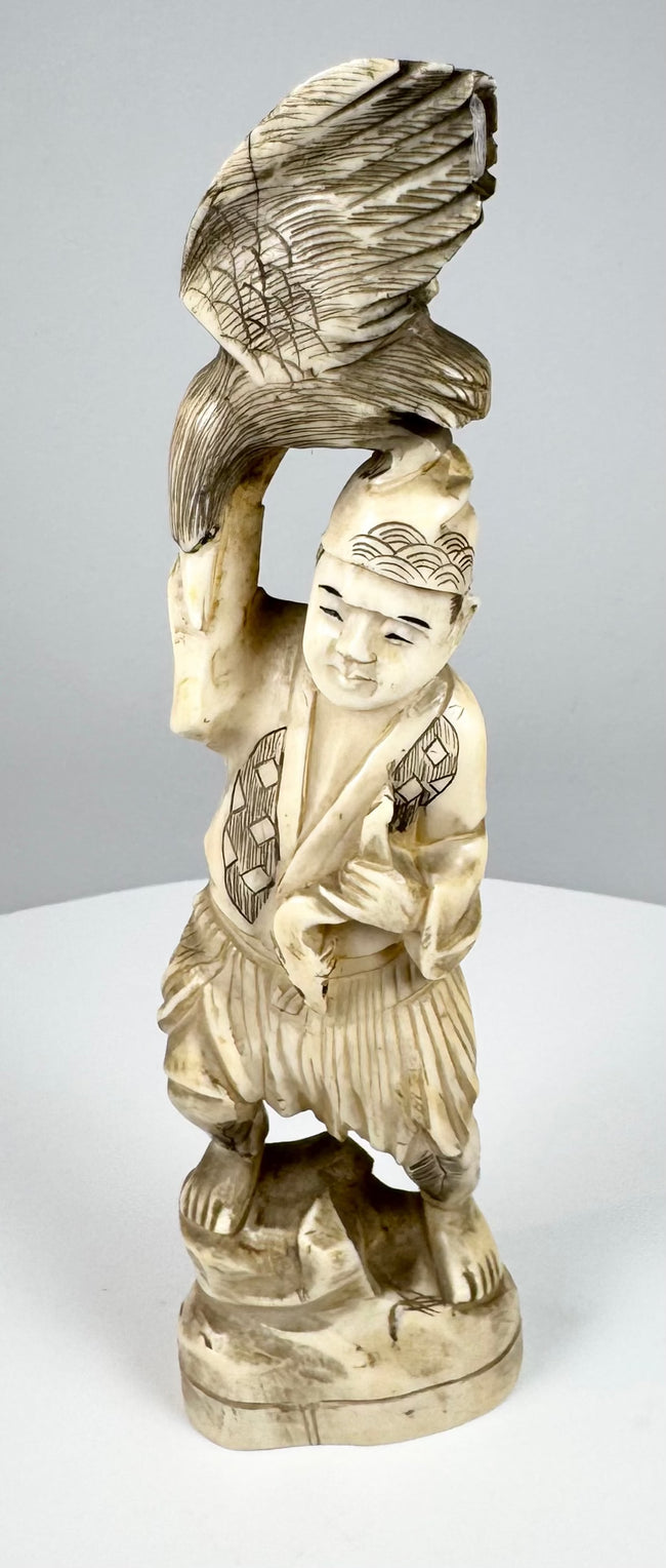Side view of a Japanese carved falconer supporting a bird of prey above his head
