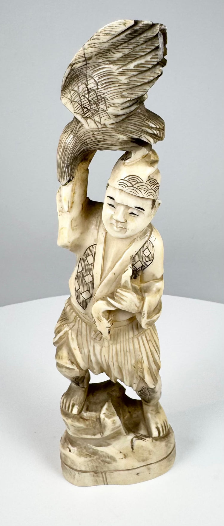 Side view of a Japanese carved falconer supporting a bird of prey above his head
