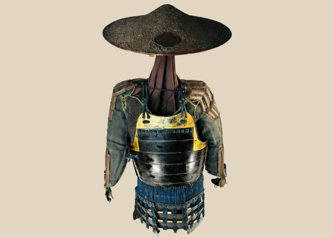 Authentic Japanese samurai armor from the Muromachi Period (1333–1573), featuring black-lacquered cuirass with gold accents, kote sleeves with chainmail reinforcement, dark-blue silk lacing, and a lacquered jingasa war hat bearing the Takeda clan crest, displayed on a wooden stand.