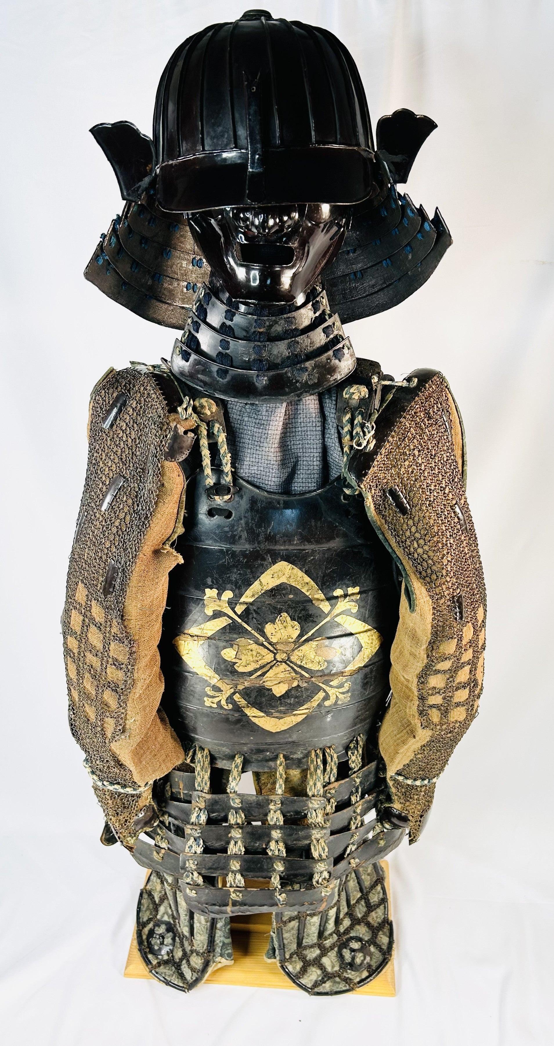 Authentic Japanese samurai armor set from the Muromachi Period (1333–1573), featuring a black-lacquered 24-plate suji-bachi kabuto helmet, menpo facial armor, gold-painted mon on the cuirass, Edo-period silk lacing, and chainmail sleeves, displayed on a wooden stand against a white background