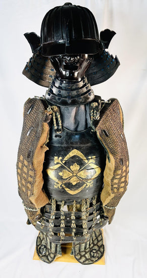 Authentic Japanese samurai armor set from the Muromachi Period (1333–1573), featuring a black-lacquered 24-plate suji-bachi kabuto helmet, menpo facial armor, gold-painted mon on the cuirass, Edo-period silk lacing, and chainmail sleeves, displayed on a wooden stand against a white background