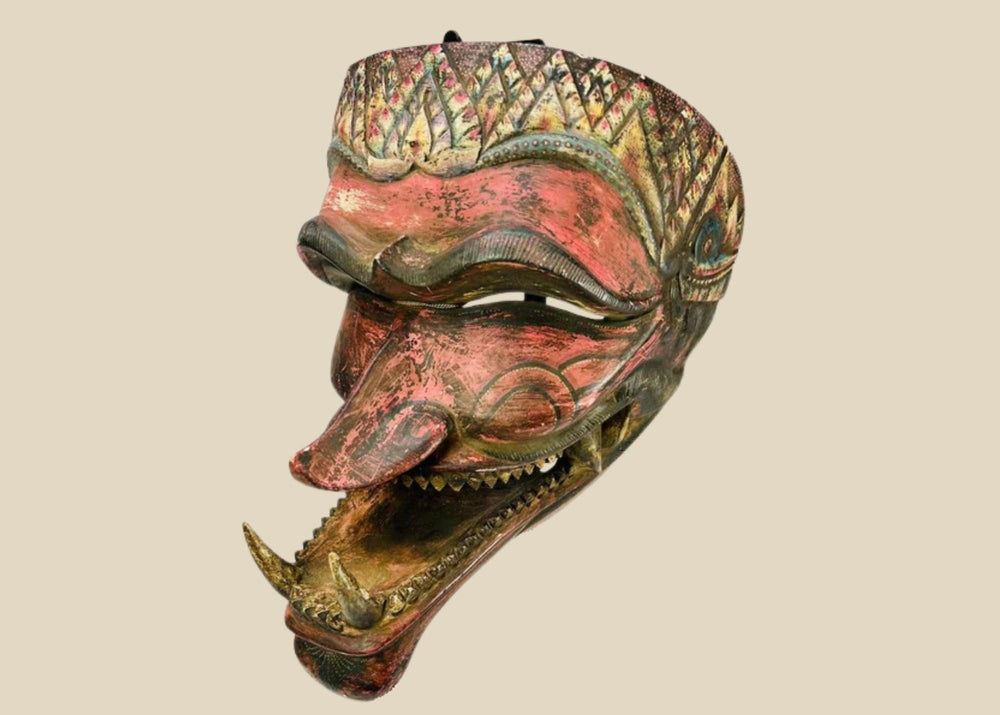 A late 19th-century Javanese carved wooden Cakil mask with sharp teeth, curved nose, crown-like decoration, and traces of red, gold, and black polychrome paint, used in Wayang Kulit performances to depict a demon antagonist.