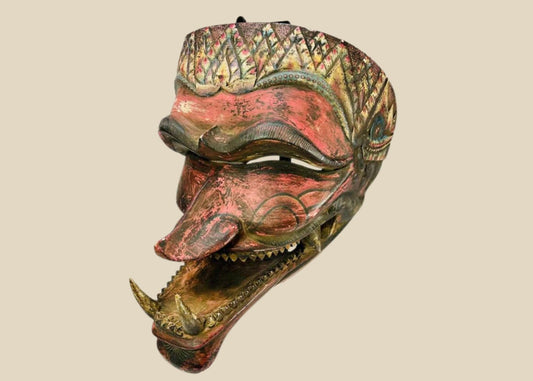 A late 19th-century Javanese carved wooden Cakil mask with sharp teeth, curved nose, crown-like decoration, and traces of red, gold, and black polychrome paint, used in Wayang Kulit performances to depict a demon antagonist.