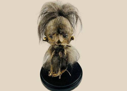 Museum-quality shrunken head replica inspired by Jivaroan tribes of the Amazon, crafted from stitched animal hide with real horse hair, detailed facial stitching, and displayed in a protective glass globe, modern creation in traditional style.