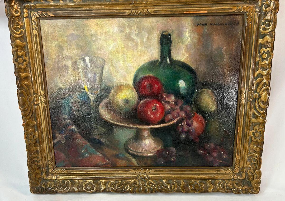 Early 20th-century American oil on canvas still life by John Hubbard Rich, depicting apples, grapes, a wine bottle, and goblet in a giltwood frame, photographed against a white background.