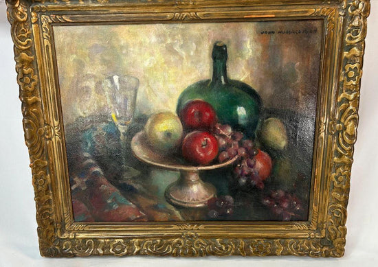 Early 20th-century American oil on canvas still life by John Hubbard Rich, depicting apples, grapes, a wine bottle, and goblet in a giltwood frame, photographed against a white background.