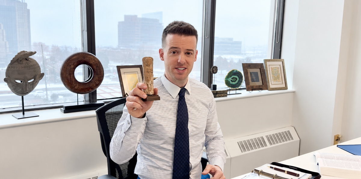 Jordan Thomas, Head Curator of Relic & Rarity, seated in the gallery office holding a small carved historical artifact.