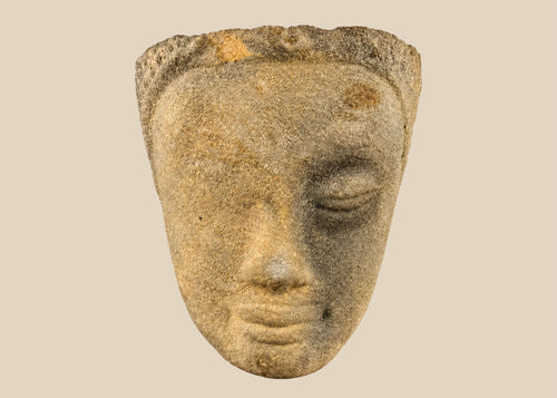 Khmer sandstone head fragment from the Angkor Period, 12th century Cambodia, depicting a serene deity or Buddha with downcast eyes and soft expression, mounted on a wooden display base, photographed on a white background.