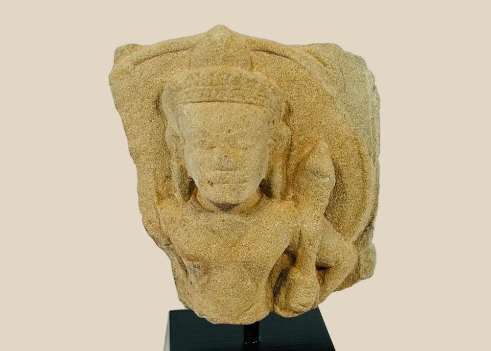 Carved stone fragment of Padmapani (Avalokitesvara) from 12th-century Khmer Empire, Cambodia, showing serene facial features and flowing contours, mounted for display.