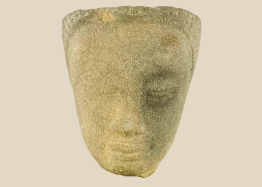 Khmer sandstone head fragment from the Angkor Period, 12th century Cambodia, depicting a serene deity or Buddha with downcast eyes and soft expression, mounted on a wooden display base, photographed on a white background.