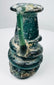 Late Roman green glass vessel showing applied handle, rounded body, and heavy burial deposits